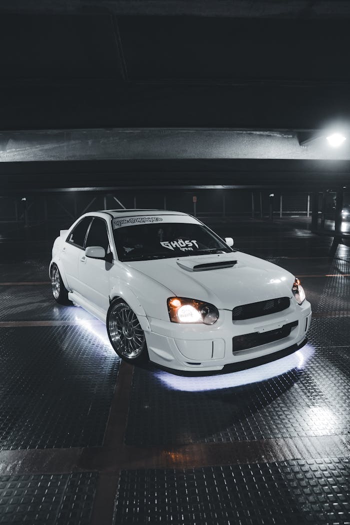 our-services-2 A sleek white Subaru sports car with neon underglow lights in a dimly lit parking garage.