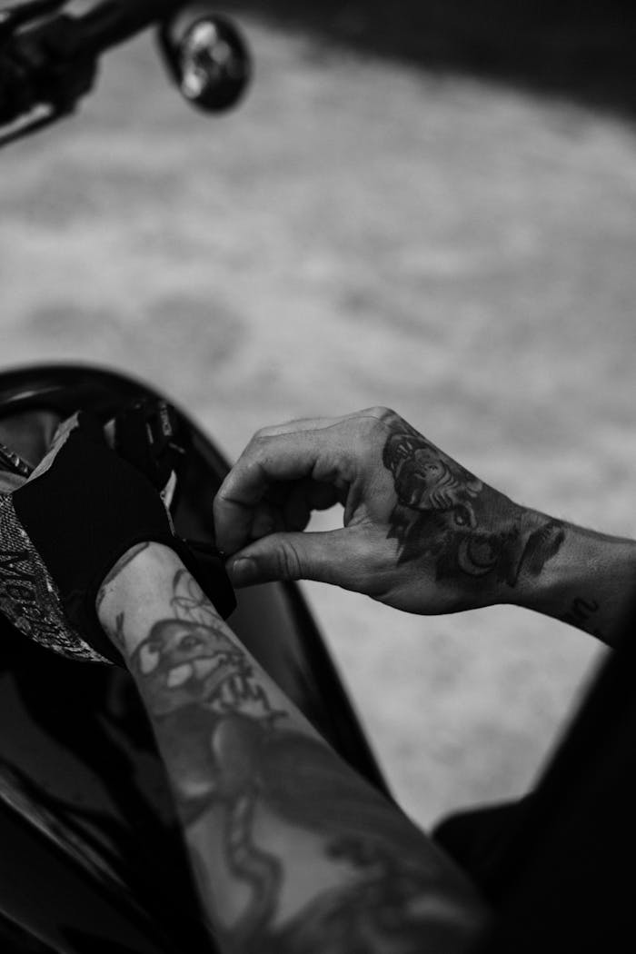 gallery-1 Artistic black and white image of a tattooed hand adjusting a glove on a motorcycle.